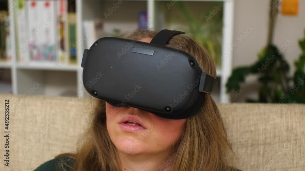 Close-up of a woman wearing virtual reality glasses sitting on the couch at home. VR helmet for entertainment, learning and gaming Close-up of a woman wearing virtual reality glasses sitting on the couch at home. VR helmet for entertainment, learning and gaming