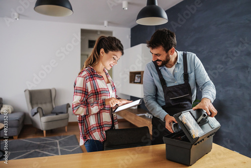Smiling housewife paying repairman over tablet while repairman collecting his tools.