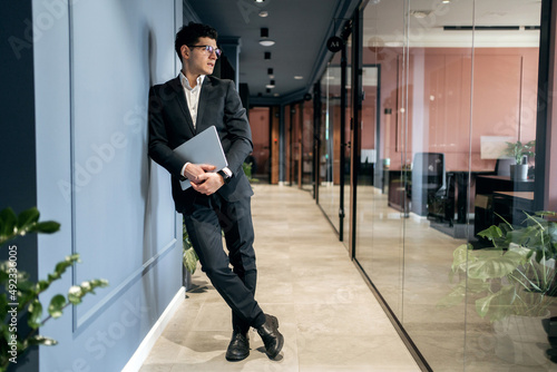 A financier man in a formal suit stands in an office coworking space