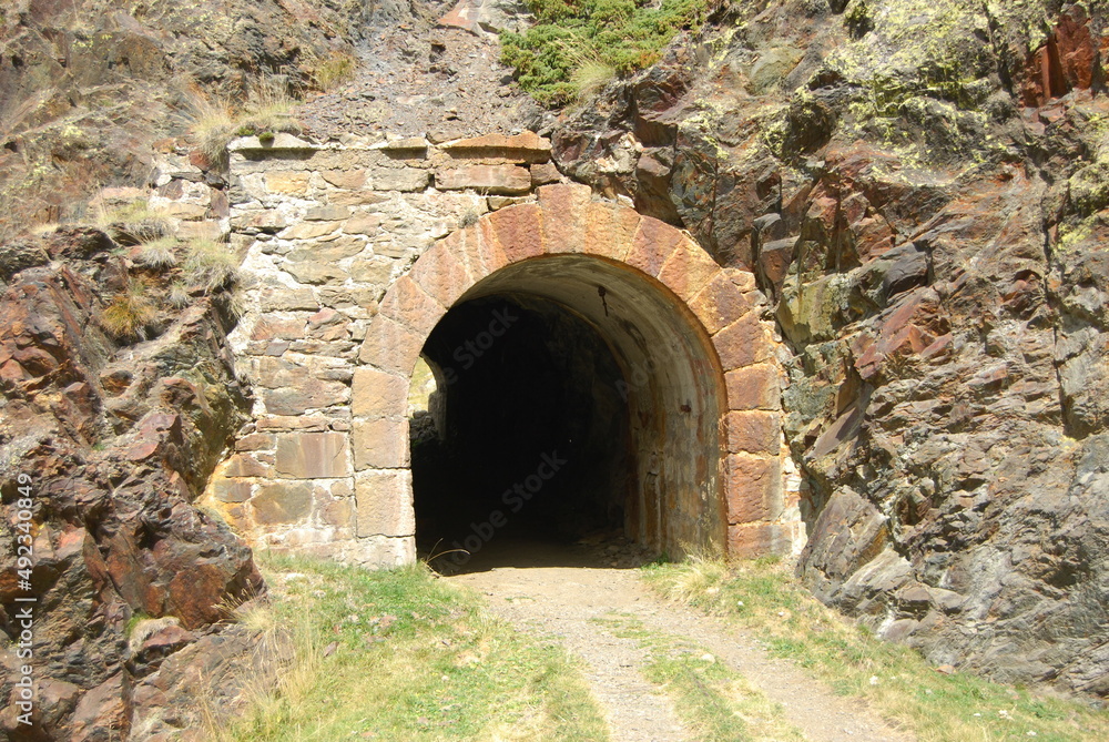 imagen de un túnel en la montaña y un camino de tierra, con la pared de piedra y rocas 