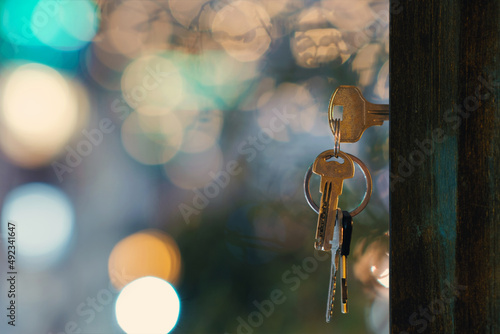 The keys with keyring in the door keyhole with blurred night lights background, selective focus