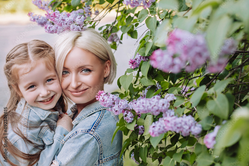 Fototapeta premium Portrait of mother and daughter close up on a lilac background. Young mother with baby having fun in the park near lilac.