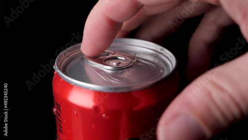 Caucasian hand opens a red soft drink can in slow motion, black background