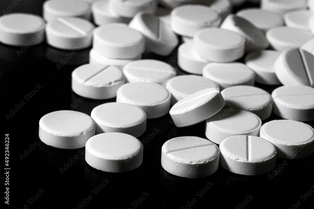 Close up of white painkiller tablet on a reflective black background Close up of white painkiller tablet on a reflective black background