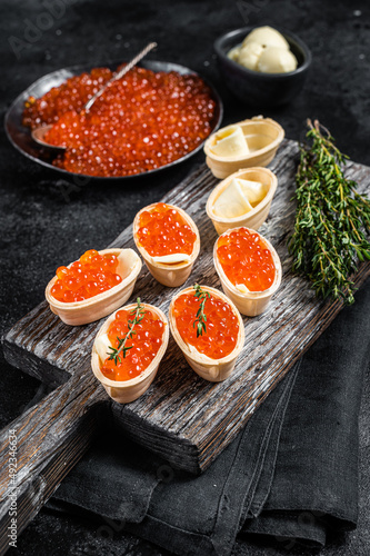 Tartlets with Red caviar, butter and thyme on wooden board. Black background. Top view