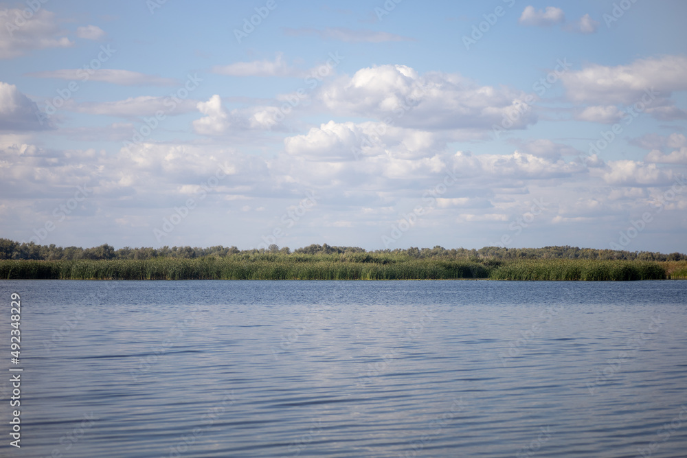Nice panoramic view of lake with ripples on water and clear blue sky with few white gray clouds drifting along background. Closer to nature away from city. 