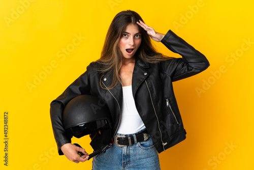 Woman holding a motorcycle helmet isolated on yellow background with surprise expression