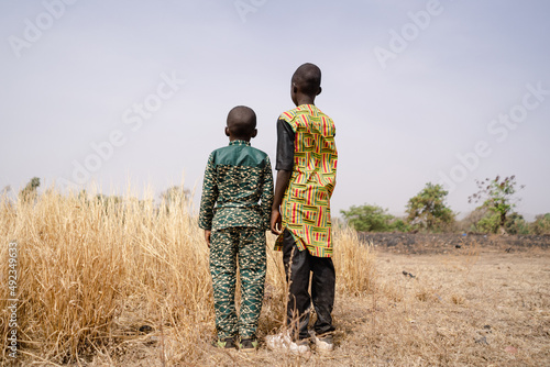 Fotografia Rear view of two African boys standing in front of a barren field with tall dry