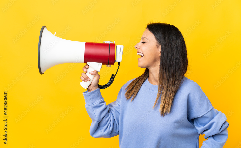 Caucasian girl isolated on yellow background shouting through a megaphone to announce something in lateral position Caucasian girl isolated on yellow background shouting through a megaphone to announce something in lateral position