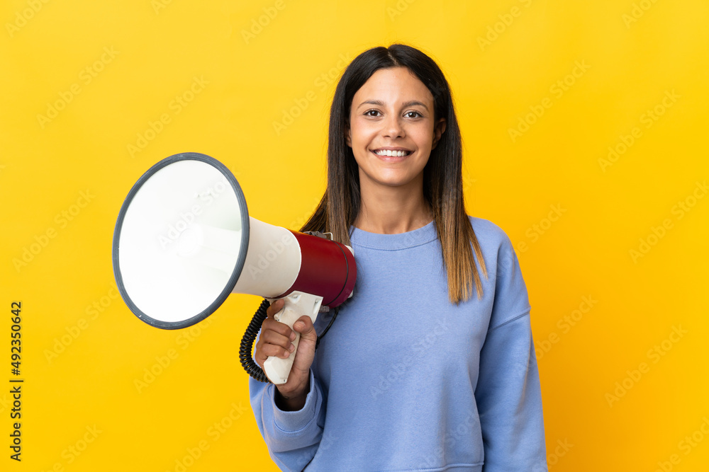 Caucasian girl isolated on yellow background holding a megaphone and smiling a lot Caucasian girl isolated on yellow background holding a megaphone and smiling a lot