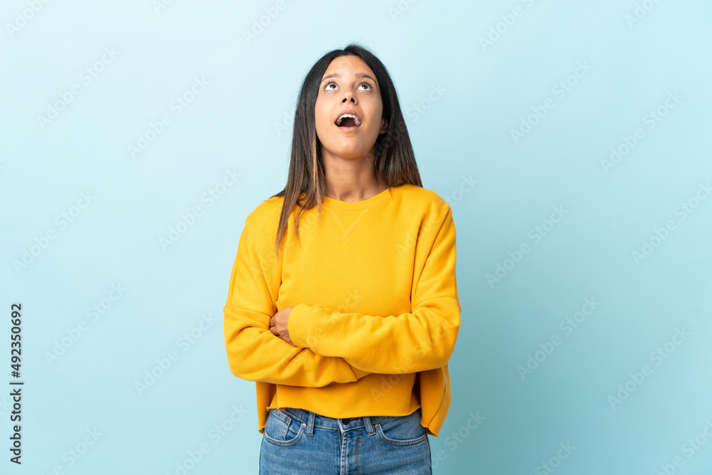 Caucasian girl isolated on blue background looking up and with surprised expression Caucasian girl isolated on blue background looking up and with surprised expression