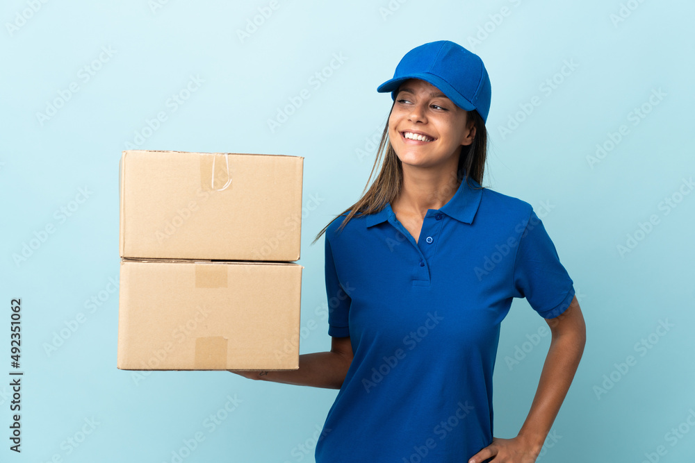 Young delivery woman isolated on blue background looking to the side and smiling Young delivery woman isolated on blue background looking to the side and smiling