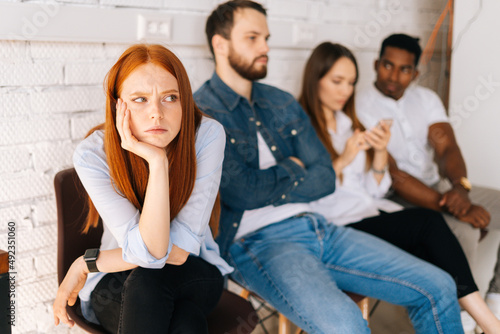 Anxious young woman job candidates looking away while waiting interview with hr sitting in queue line row with bored diverse multi-ethnic competitors, on background of white brick wall.