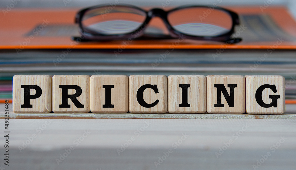 Obraz premium PRICING - word on wooden cubes on the background of a folder with documents and glasses