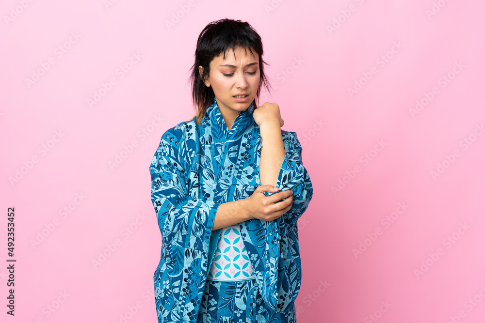 Young woman wearing kimono over isolated blue background with pain in elbow Young woman wearing kimono over isolated blue background with pain in elbow