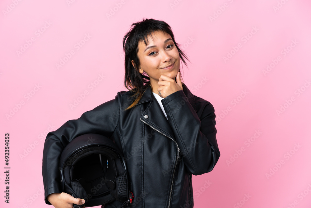 Young Uruguayan woman holding a motorcycle helmet over isolated pink background laughing Young Uruguayan woman holding a motorcycle helmet over isolated pink background laughing