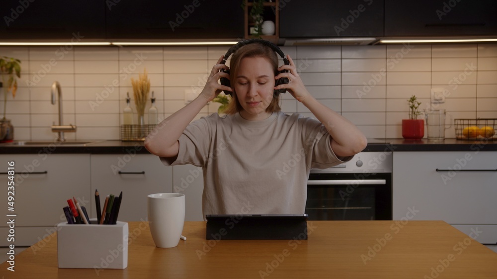 Portrait of a happy girl putting on headphones in the living room at the table Portrait of a happy girl putting on headphones in the living room at the table