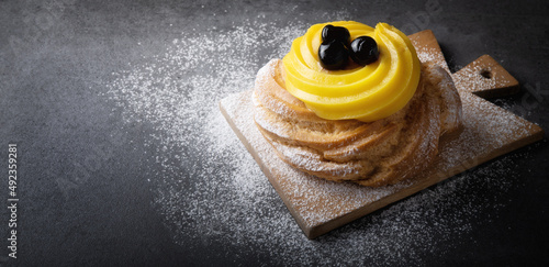 Italian dessert, Zeppola di San Giuseppe, baked cake garnished with custard and sour cherries in syrup, on gray background, space for text, close-up.. photo