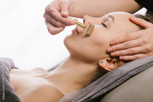 Roller gua sha massage of a woman in a beauty salon over white background.