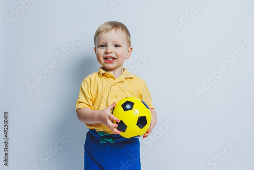 A little boy with a soccer ball in his hands on a white background, a child is a novice football player, a sport for children. Little athlete. Yellow and blue football kit for kids
