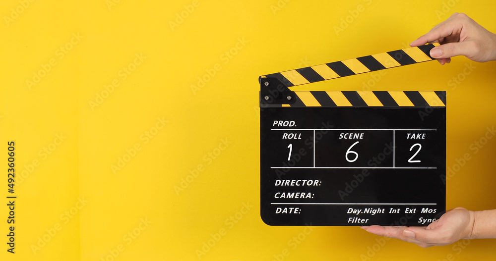 Hands are holding black and yellow clapper board or movie slate with a number on yellow background..