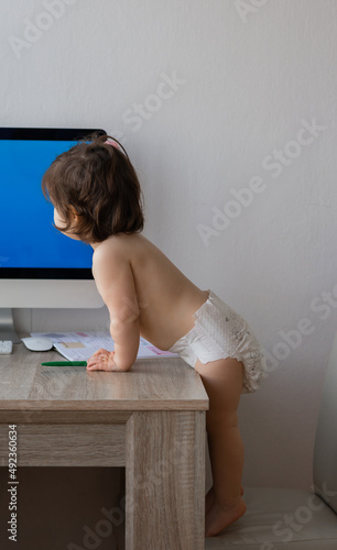 Baby toddler in diaper looking at screen of pc.
