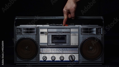 A man's hand with a finger presses the play button on an old vintage gray cassette tape recorder