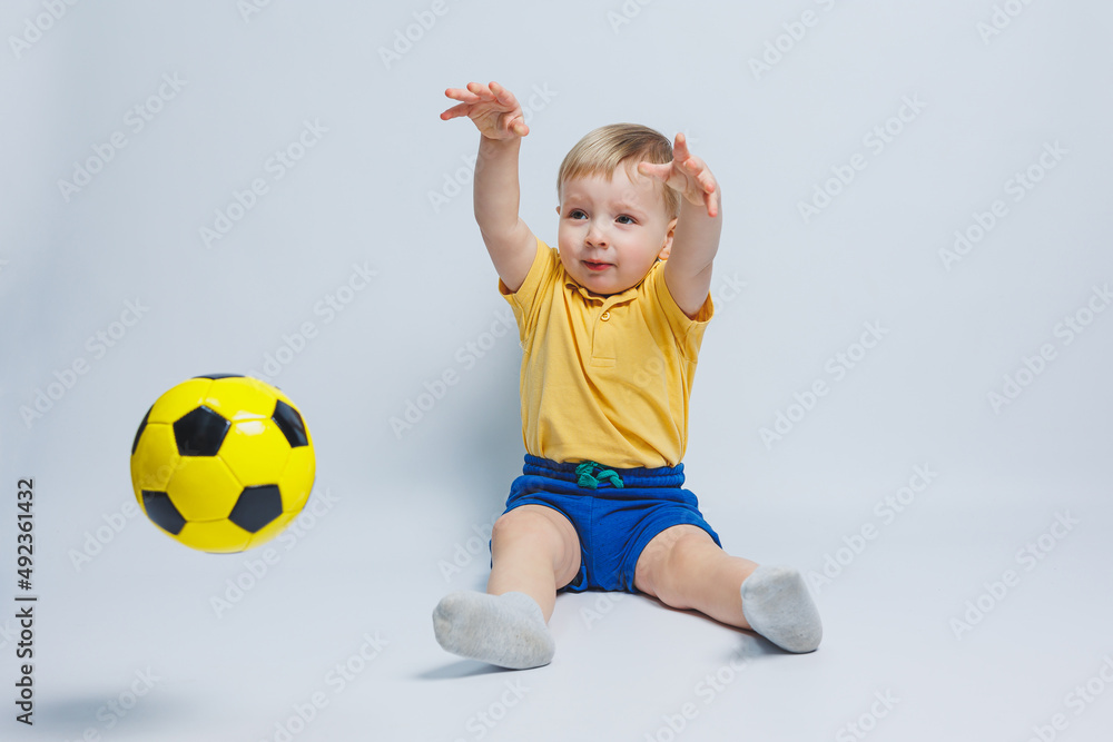 Cheerful little boy 5-6 years old football fan in a yellow T-shirt, supports the team, holds a soccer ball in his hands, isolated on a white background. The concept of sports family recreation Cheerful little boy 5-6 years old football fan in a yellow T-shirt, supports the team, holds a soccer ball in his hands, isolated on a white background. The concept of sports family recreation