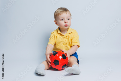 Cheerful little boy 5-6 years old football fan in a yellow T-shirt, supports the team, holds a soccer ball in his hands, isolated on a white background. The concept of sports family recreation
