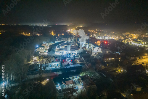 Panorama małego prowincjonalnego miasta w nocnej scenerii. W centrum kadru widać jaskrawo oświetloną fabrykę. Zdjęcie z wysokości wykonane z użyciem drona.