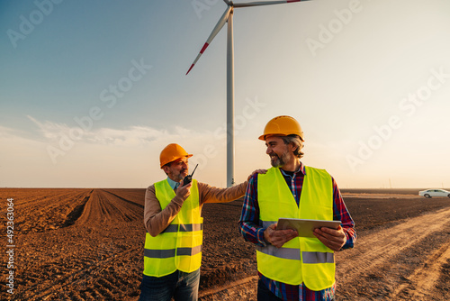 Men checking wind turbines at field and using technology