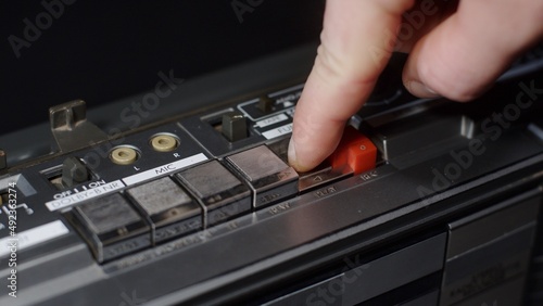 A man's hand with a finger presses the play button on an old vintage gray cassette tape recorder