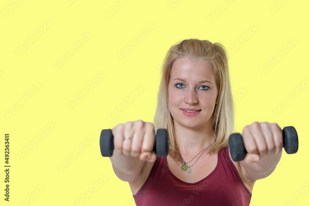 Studio shot of attractive young woman posing with a dumbbells on yellow background. Studio shot of attractive young woman posing with a dumbbells on yellow background.