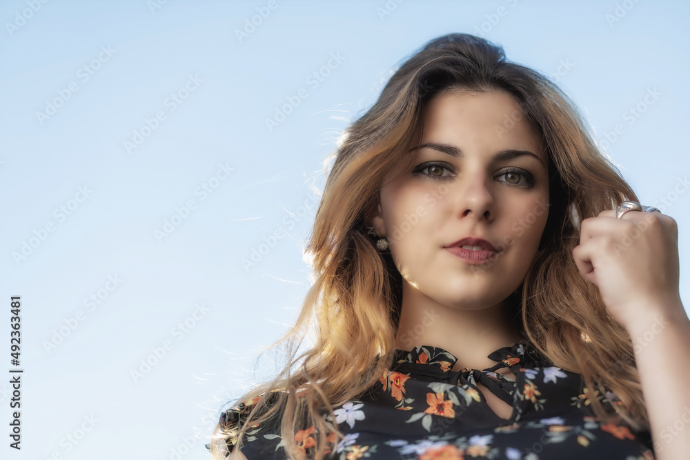 Fototapeta premium Portrait of cool beautiful young woman iposing outdoors against blue sky.