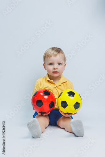 Little european boy, fan or player in yellow and blue uniform with a soccer ball, supports the soccer team on a white background. Football sport game, lifestyle concept. Isolated on white background