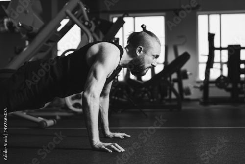 A young man with a beard does a push-up exercise in the gym. Black and white photography