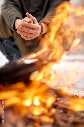 Man warming hands on bonfire in nature in cold season, winter. travel lifestyle photo. adventure active vacations outdoor. Extreme camping. in snowy frozen forest alone. close-up focus on hands