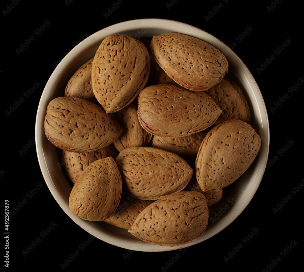 Almond nuts in shells, kernels in bowl isolated on black, top view Almond nuts in shells, kernels in bowl isolated on black, top view
