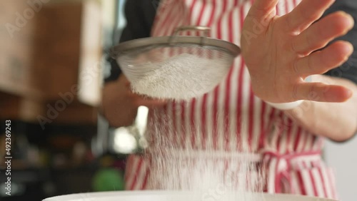 Woman baker sifting flour for dough through bolter photo