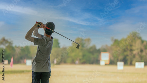 Young man is practicing his golf swing at the golf driving range.