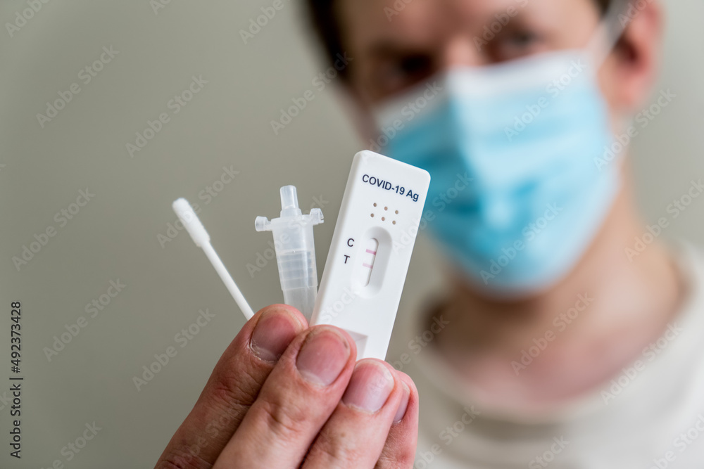 Man wearing face mask holding Covid-19 rapid antigen test kit and cassette with positive result of rapid diagnostic test. Man wearing face mask holding Covid-19 rapid antigen test kit and cassette with positive result of rapid diagnostic test.