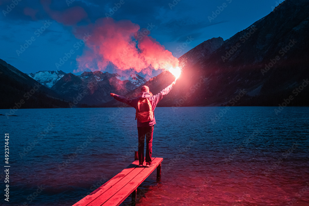 The hiker on the pier lit the emergency red torch and calling for help. Rescue flare and sos signal concept