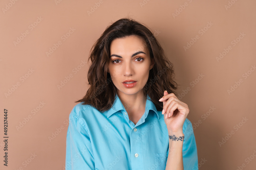 Young woman with wavy voluminous hair and natural daytime make-up wearing a blue shirt on a beige background Young woman with wavy voluminous hair and natural daytime make-up wearing a blue shirt on a beige background