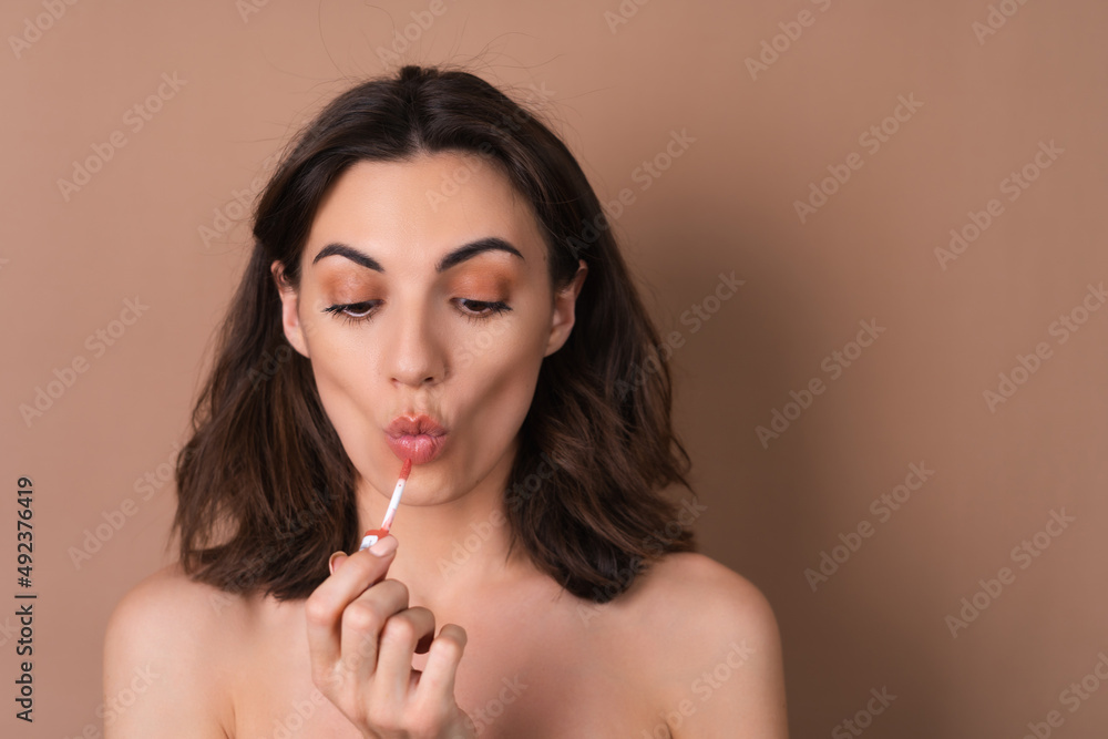 Beauty portrait of topless woman with perfect skin and natural make-up on beige background holding brown chocolate gloss lipstick Beauty portrait of topless woman with perfect skin and natural make-up on beige background holding brown chocolate gloss lipstick