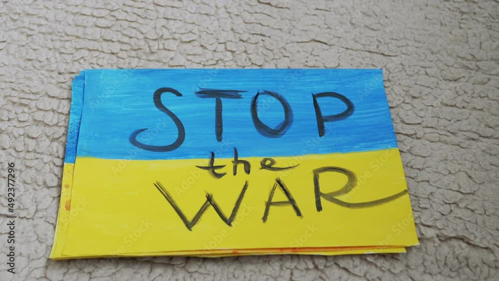 Female Hands Lay Out Drawings on the Floor with Inscriptions Stop War in Ukraine. Messages on the banner with an appeal to confront the military conflict on poster of the blue-yellow flag of Ukraine. Female Hands Lay Out Drawings on the Floor with Inscriptions Stop War in Ukraine. Messages on the banner with an appeal to confront the military conflict on poster of the blue-yellow flag of Ukraine.