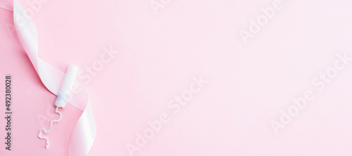 Tampon woman feminine hygiene. Pink ribbon with menstrual tampon on pink background. Menstruation feminine period. Soft tender protection for women critical days.