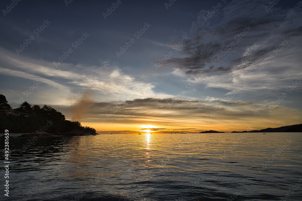 Fototapeta premium Dramatic sunset over sea with clouds in the sky and mountain in background - Thailand Koh Lipe