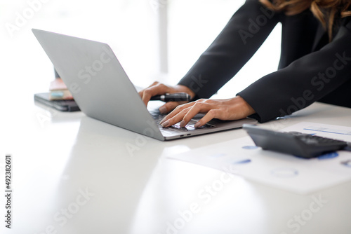 Charming Asian businesswoman sitting in the office with a digital laptop computer. Excited Asian businesswoman raising hands to congratulate while working in a modern office 