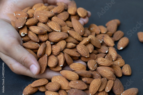 Delicious roasted sweet almonds lie in a large heap, nuts close-up.Almonds seed in hand on Black Background
