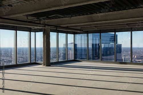 Fototapeta Naklejka Na Ścianę i Meble -  Corner of empty office space with floor to ceiling windows and view over sprawling urban area